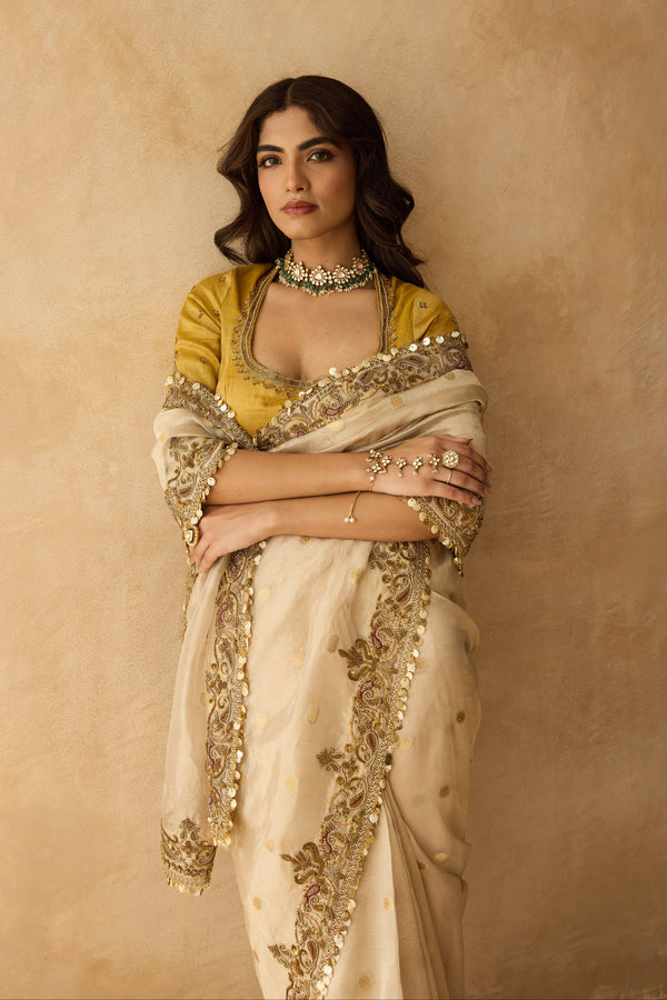 Woman in a traditional outfit with gold and beige colors against a beige background
