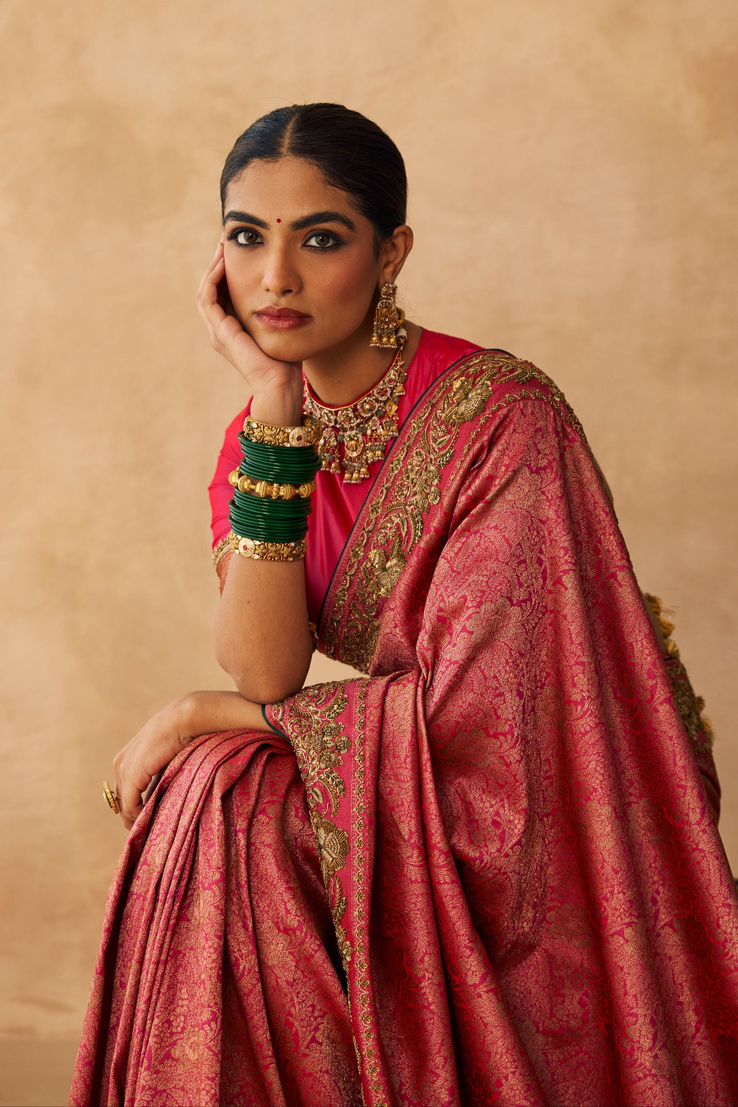 Woman in a pink saree with gold details against a beige background