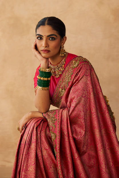 Woman in a pink saree with gold details against a beige background