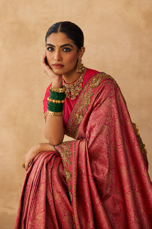 Woman in a pink saree with gold details against a beige background