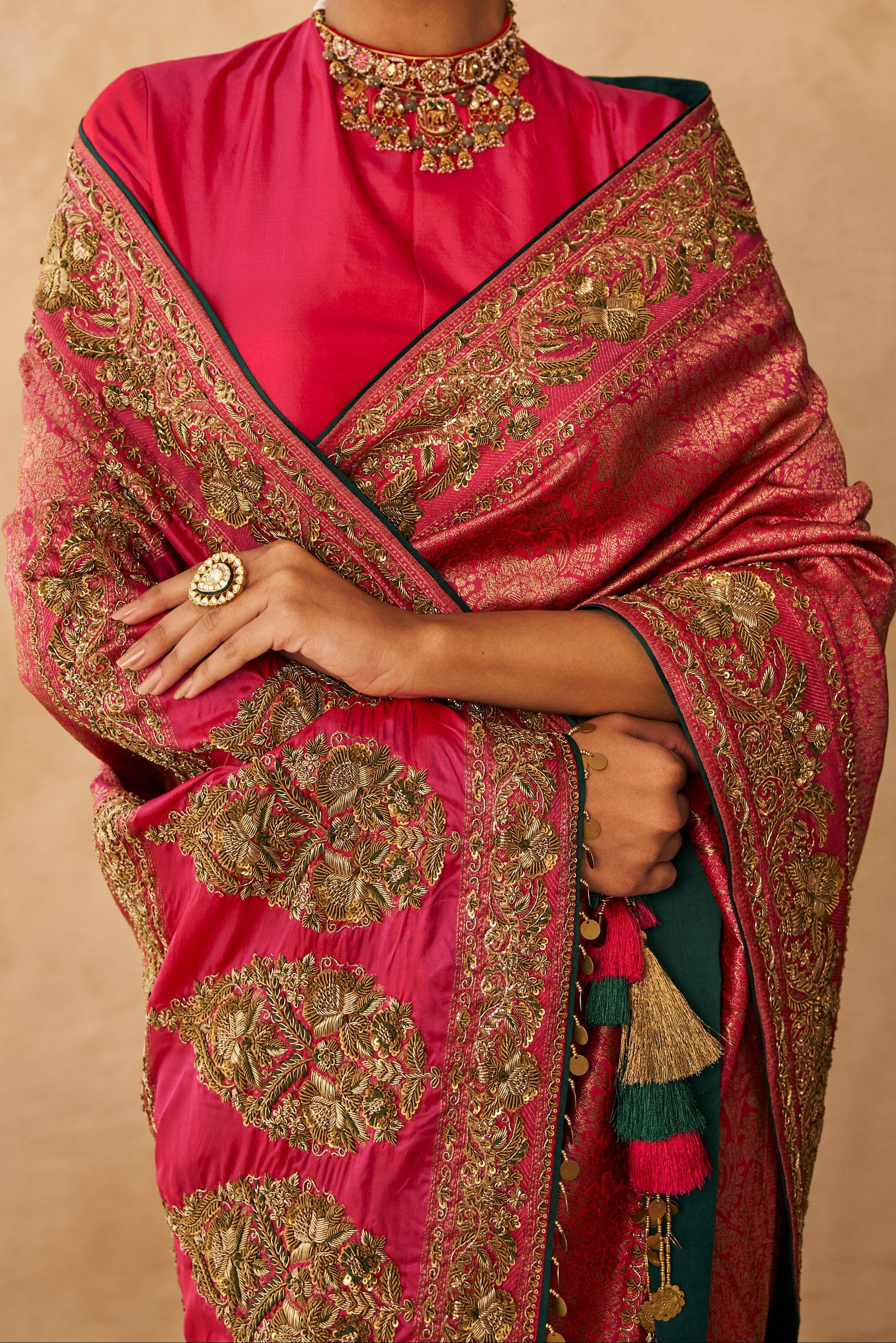 Woman wearing a pink saree with gold patterns against a beige background