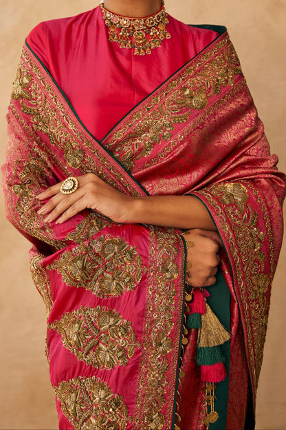 Woman wearing a pink saree with gold patterns against a beige background